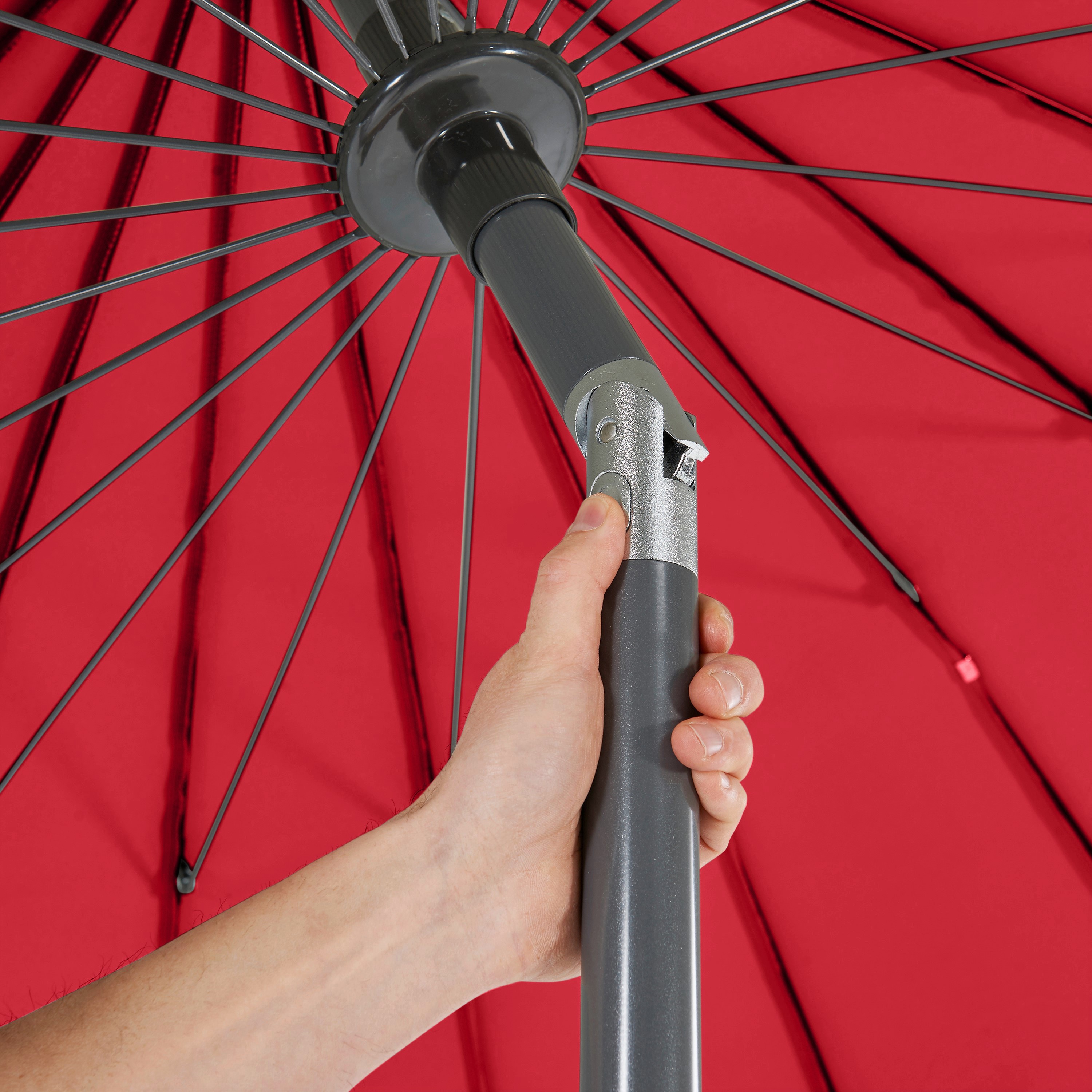 Hand hält grauen Griff eines aufgespannten roten Regenschirms mit Metallgestell.