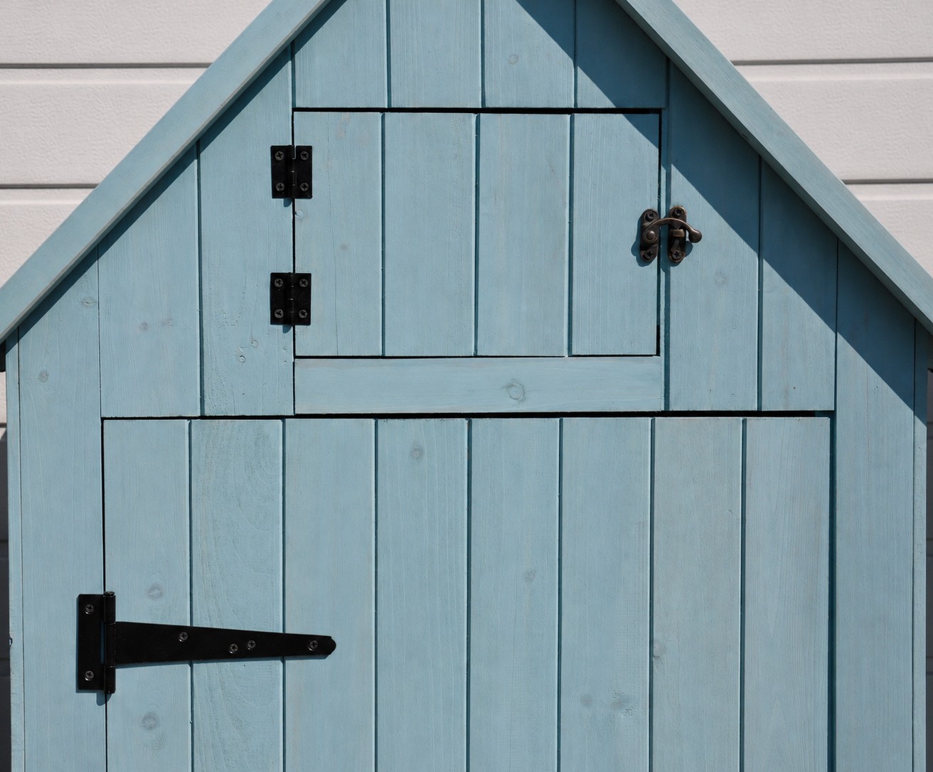 Blaue Holztür mit zwei schwarzen Scharnieren und einem Riegel, vor einer weißen Wand montiert.