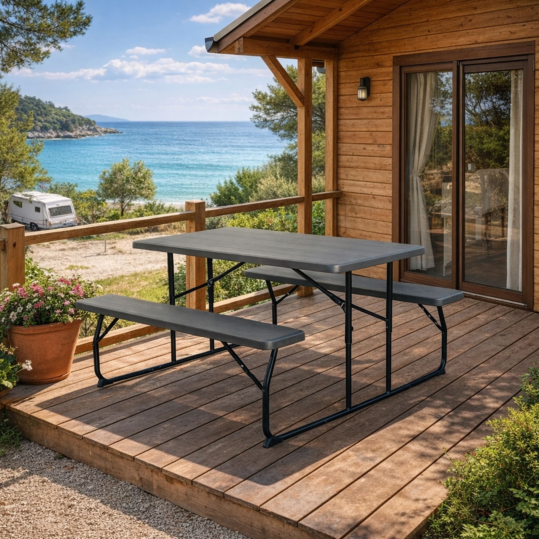 Holzterrasse mit Tischgarnitur, Blick auf Meer und Wohnmobil, umgeben von Bäumen, sonniges Wetter.