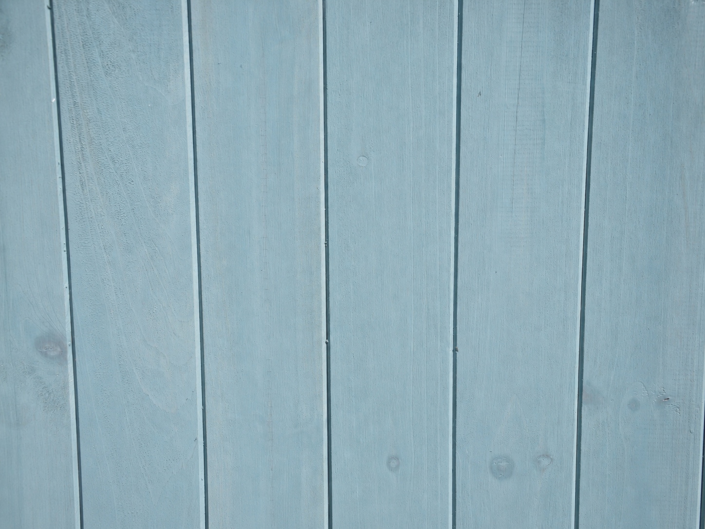 Hellblaue Holzwand mit vertikalen Paneelen und sichtbarer Maserung.